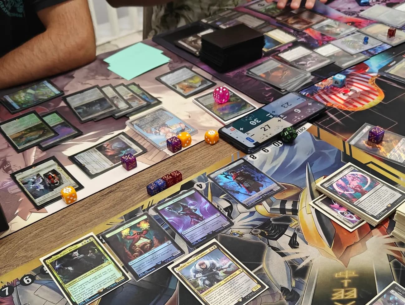Partie de Commander Magic the Gathering en cours sur une table : commandants légendaires, cartes étalées et dés de comptage des points de vie