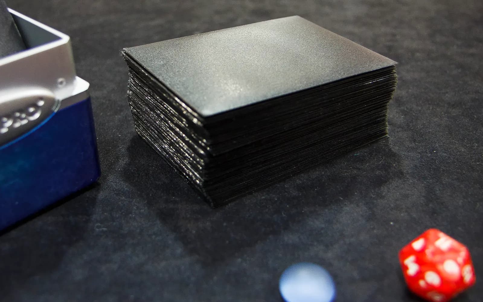 Deck de Magic the Gathering sous pochettes posé près d'une boîte de rangement, d'un dé et de jetons de jeu