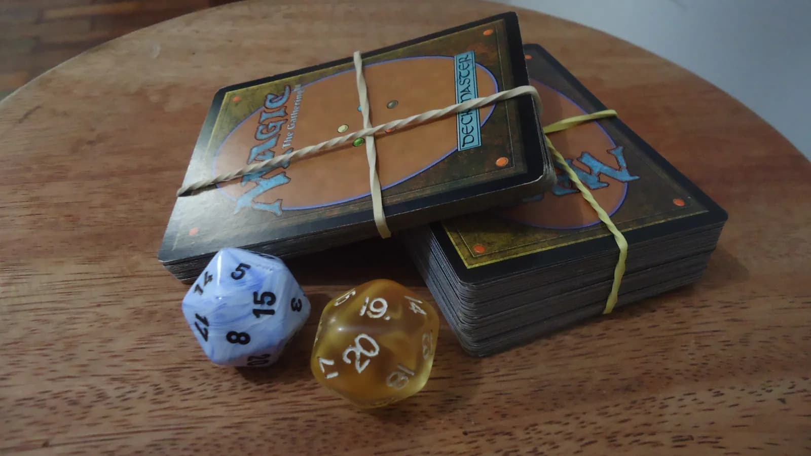 Deux paquets de cartes Magic the Gathering posés sur une table en bois, accompagnés de deux dés à vingt faces