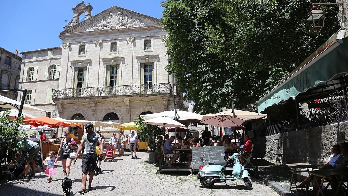 Place du centre historique de Pézenas un jour de marché, terrasses de café et façades en pierre du Languedoc