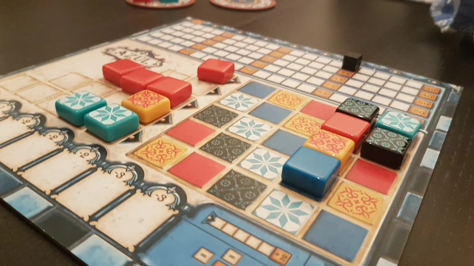 Plateau de jeu Azul en cours de partie avec les lignes de motif remplies et les fabriques disposées en arrière-plan
