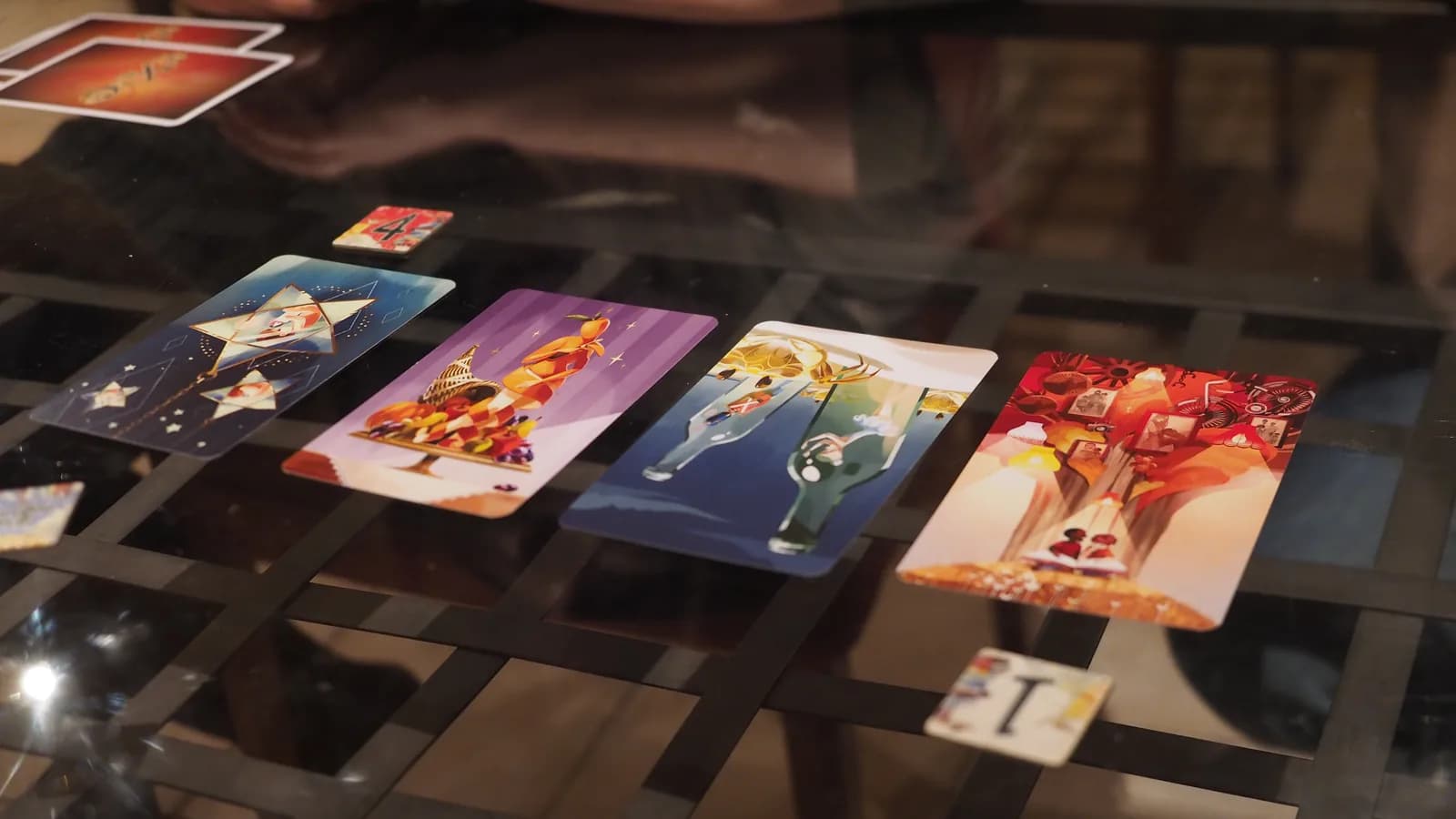 Quatre cartes illustrées de Dixit alignées sur une table en verre pendant la phase de vote, avec deux jetons numérotés visibles