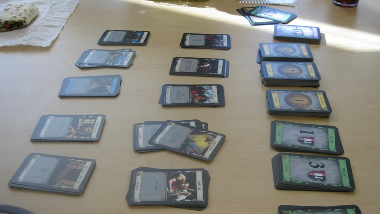 Mise en place d'une partie de Dominion : piles de cartes Action, Trésors et Points de victoire disposées sur une table en bois