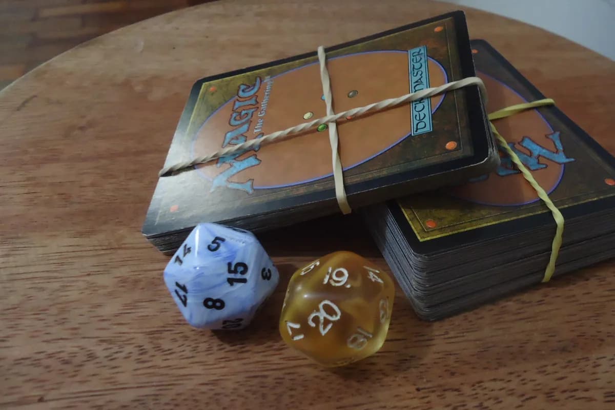 Deux paquets de cartes Magic the Gathering tenus par des élastiques, posés sur une table en bois avec deux dés à vingt faces