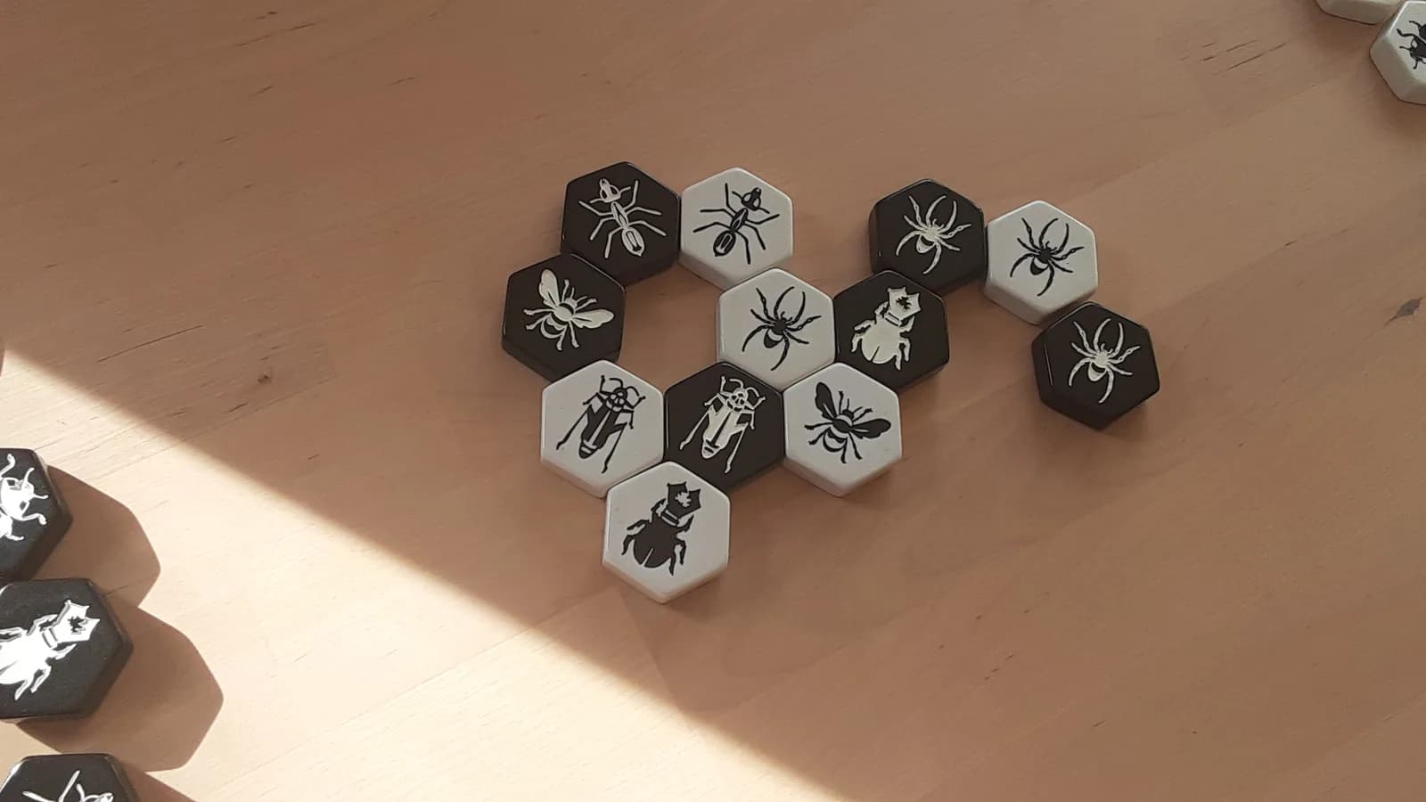 Tuiles hexagonales noires et blanches du jeu Hive formant une ruche, avec fourmi, araignée, scarabée et reine abeille